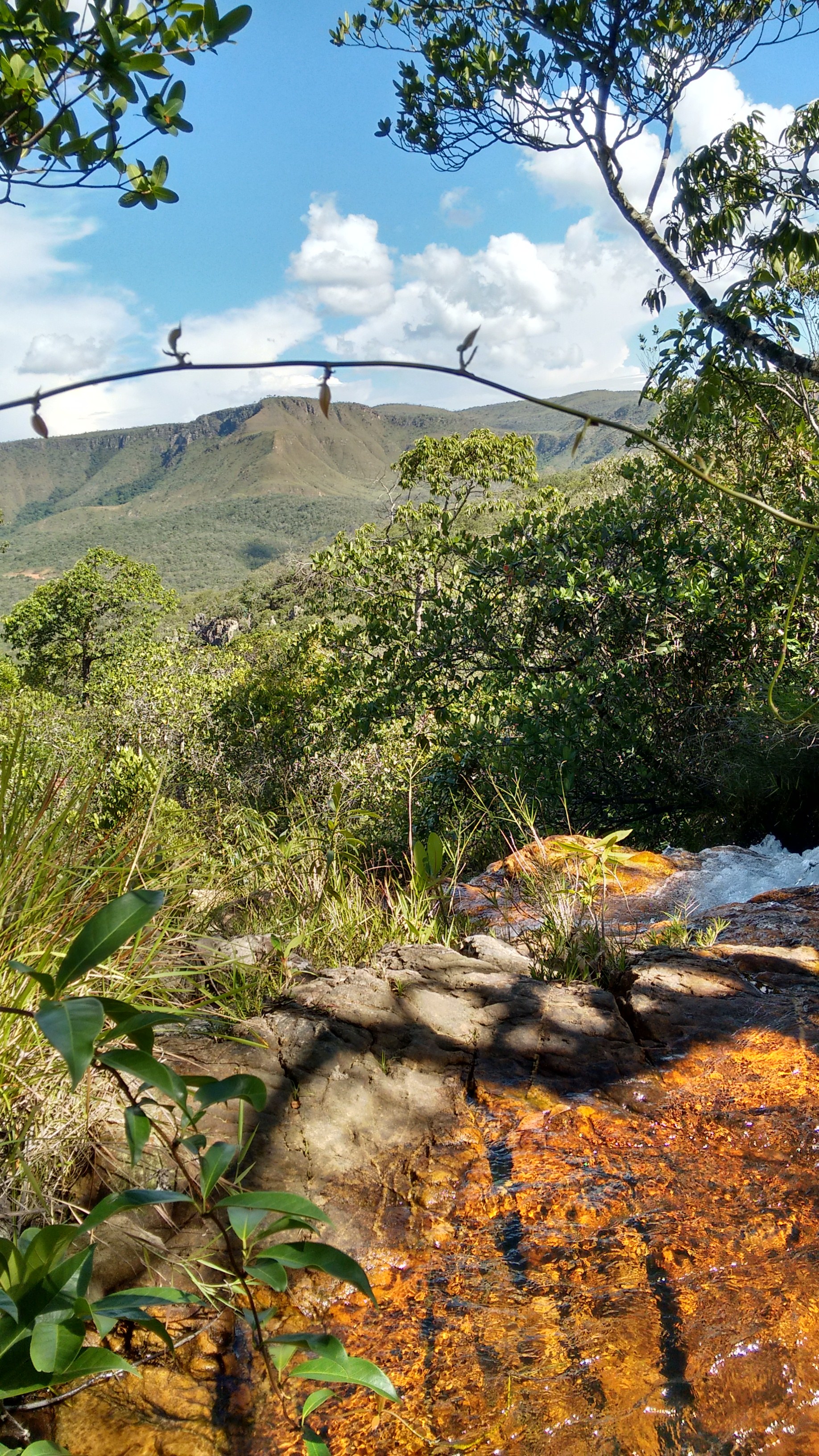 Riacho sobre laje alaranjada e o vale da Chapada dos Veadeiros ao fundo, em Goiás.